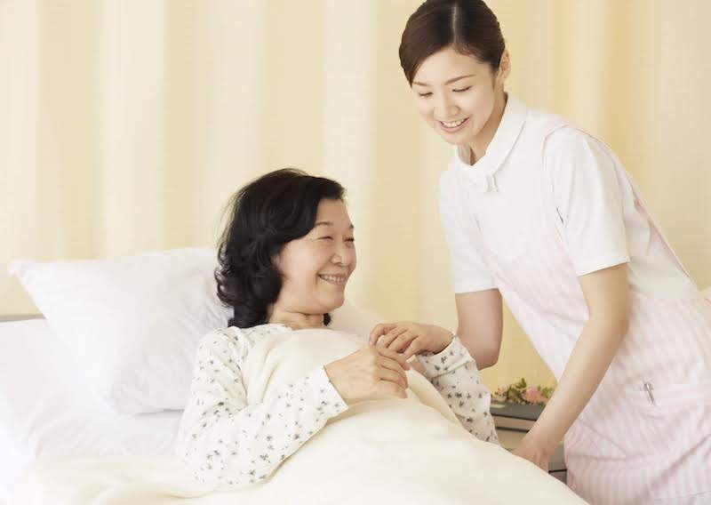 高齢の女性をベッドから起こそうと介助する女性の介護士