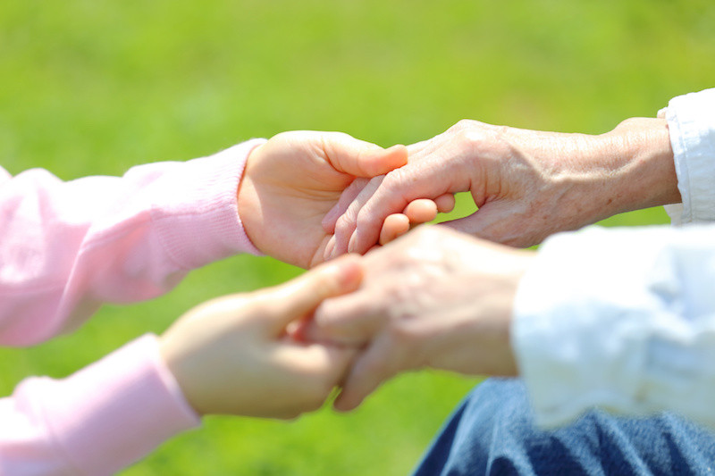 高齢者の両手を優しくつかむ介護士の手元を横から見た写真